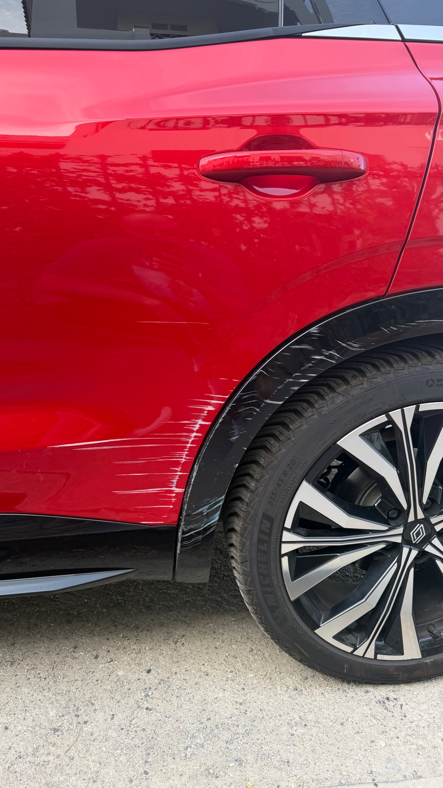 A long scrape running along the rear door and wheel arch of the red rental car