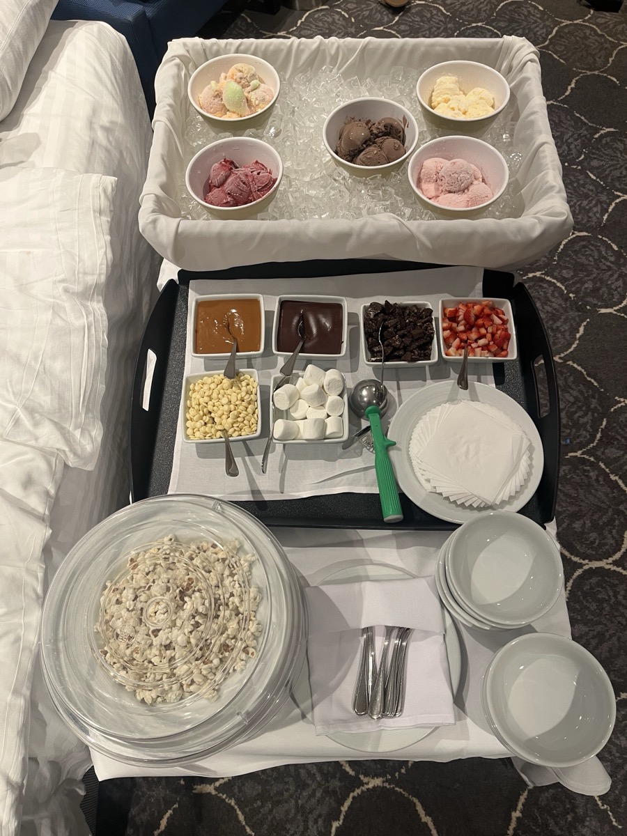 In-suite sundae bar — five flavors of ice cream on ice, six toppings on a tray, marshmallows, white chocolate chips, and a bowl of popcorn