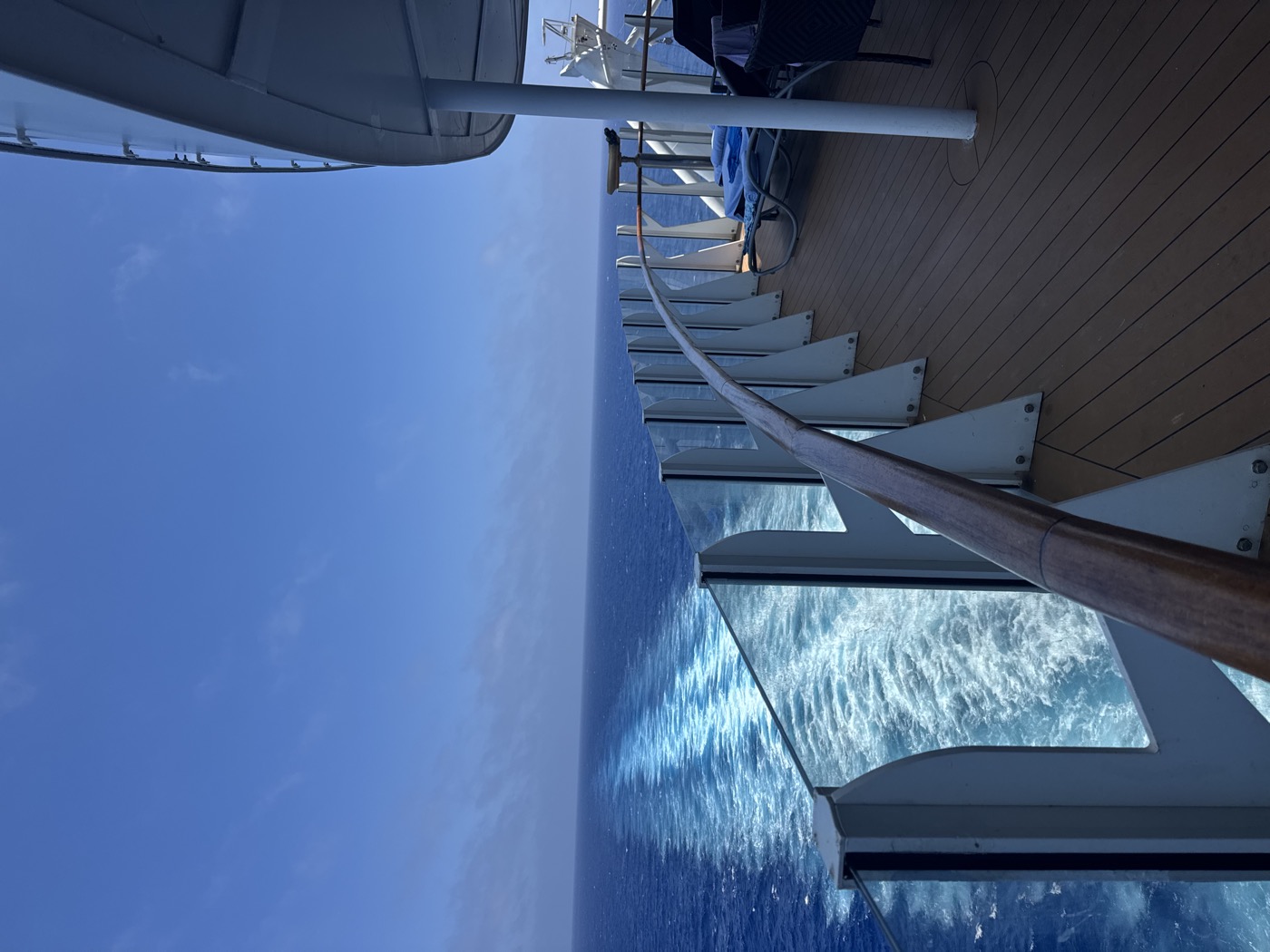 Wooden deck with empty loungers lined up along the railing, open ocean and clear sky beyond