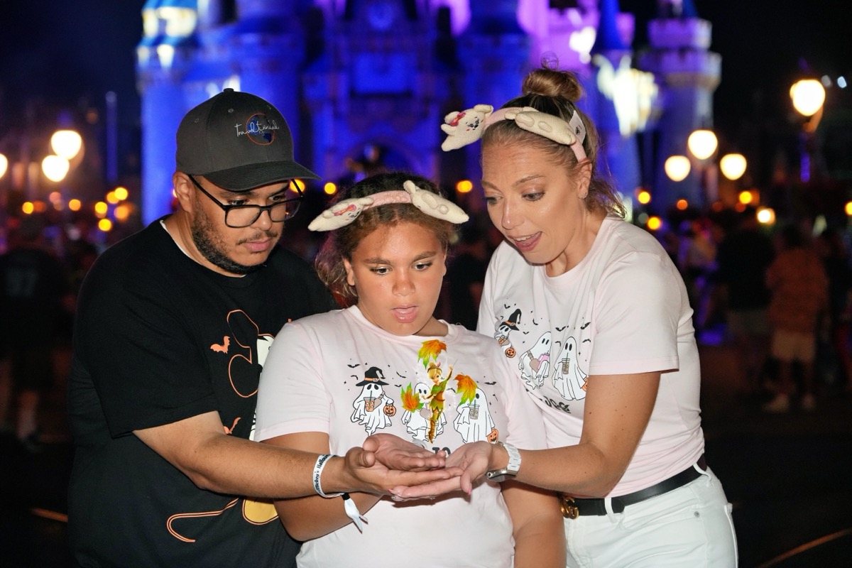 Family in matching ghost shirts in front of Cinderella Castle at night with Mickey ears