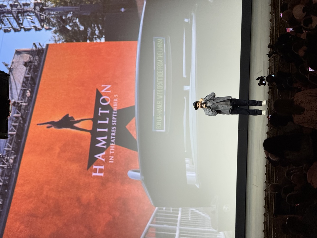 Hamilton movie premiere event with Lin-Manuel Miranda addressing the crowd in front of a giant Hamilton screen