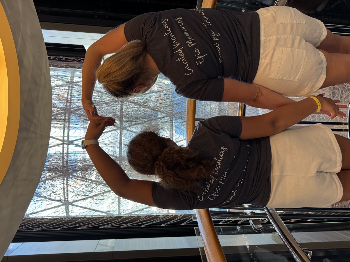 Two travelers hugging in matching Travel by Trinidad branded shirts that read "Curated Vacations, Epic Memories"