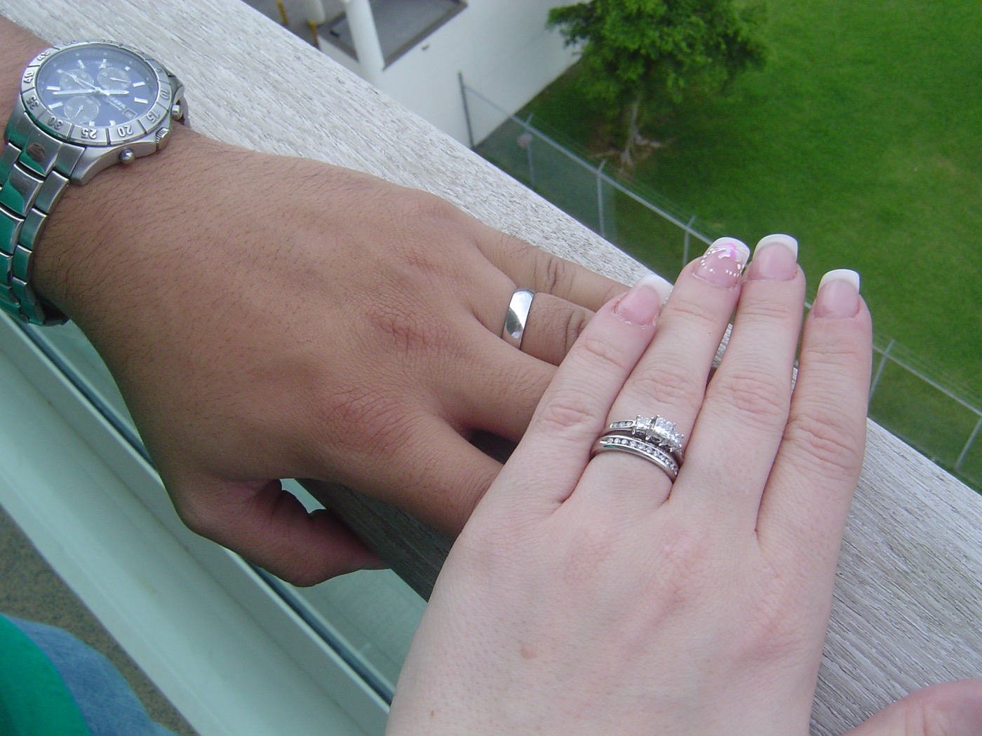 Newlywed hands resting on a balcony rail, both rings catching the light
