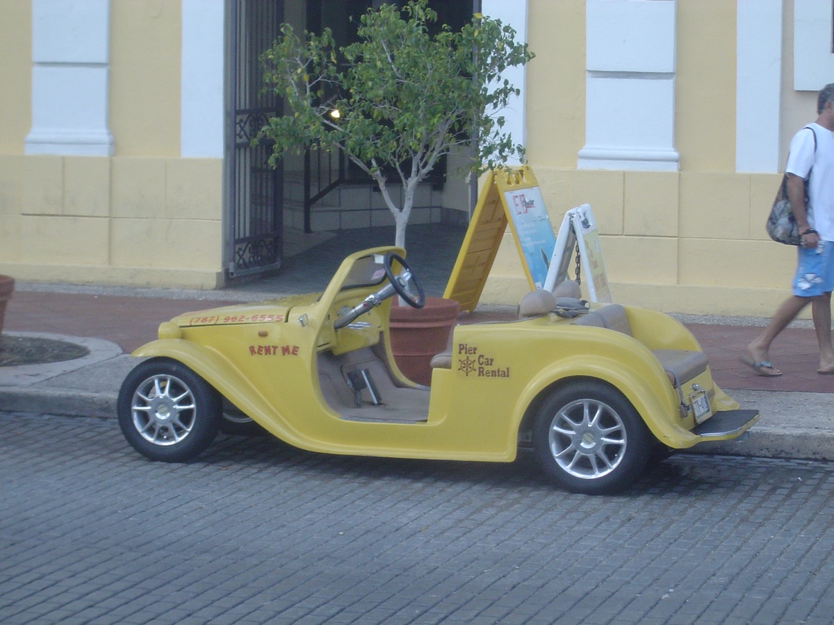Bright yellow Pier Car Rental rent-me convertible on a brick street in San Juan