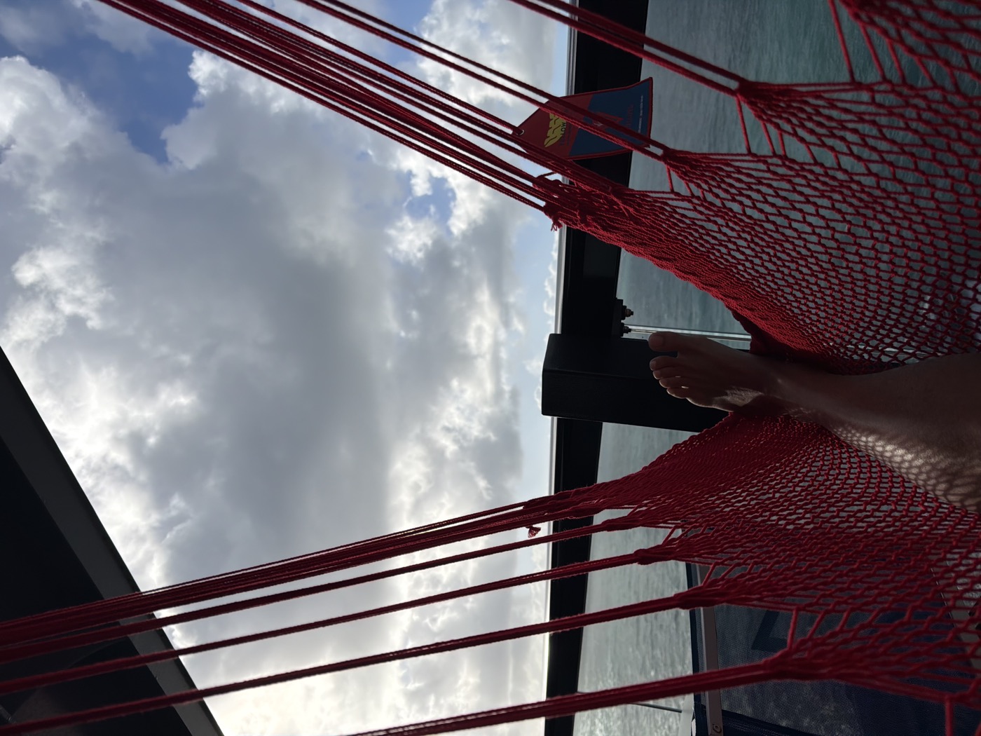 Red rope hammock on the Sea Terrace balcony, looking out at scattered clouds over open water