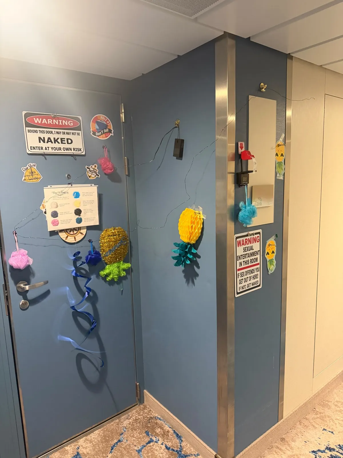 A cruise cabin door covered in tongue-in-cheek warning signs, pineapple decorations and streamers